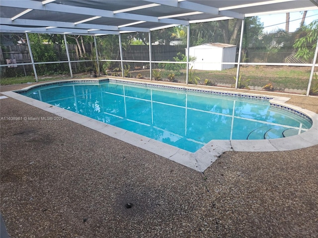 view of pool with glass enclosure and a storage shed