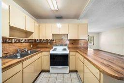 kitchen with white electric stove, light tile patterned flooring, sink, backsplash, and butcher block counters