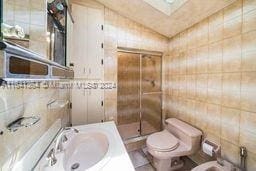 bathroom with an enclosed shower, sink, tile walls, and toilet