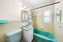 full bathroom featuring tile walls, toilet, tiled shower / bath combo, and vanity