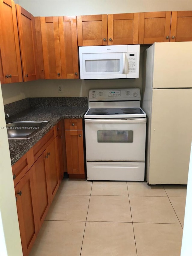 kitchen with dark stone countertops, sink, white appliances, and light tile patterned floors