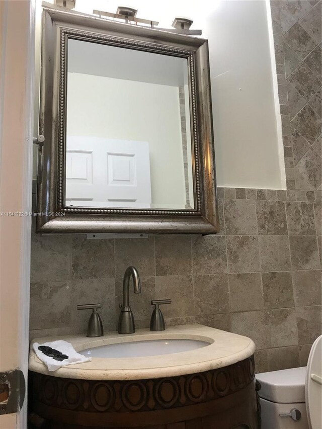 bathroom featuring backsplash, tile walls, toilet, and vanity