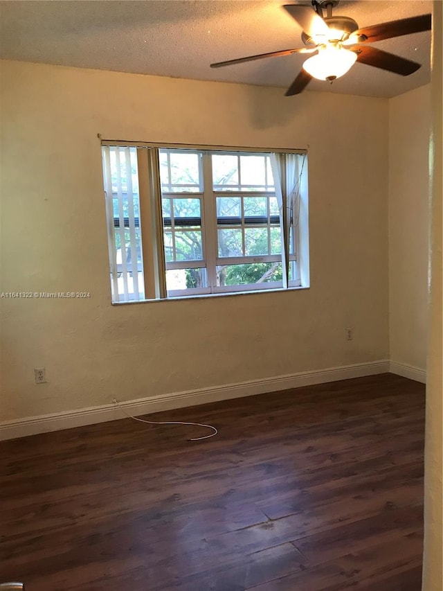 empty room featuring ceiling fan, plenty of natural light, dark wood-type flooring, and a textured ceiling