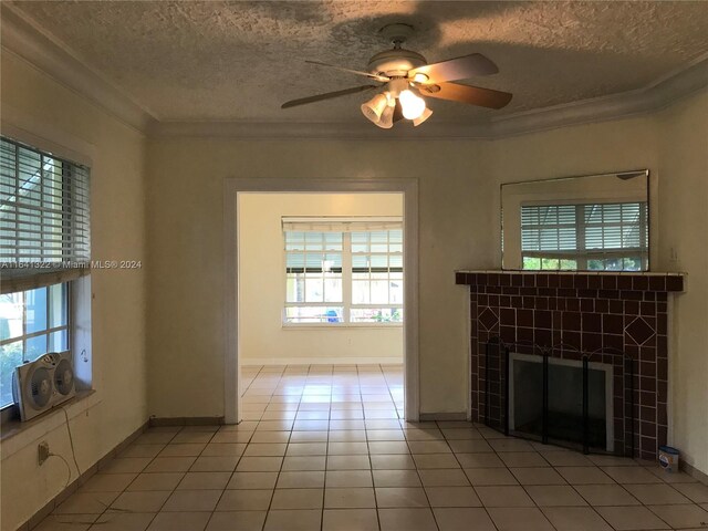 unfurnished living room featuring ceiling fan, a tile fireplace, a textured ceiling, crown molding, and light tile patterned flooring