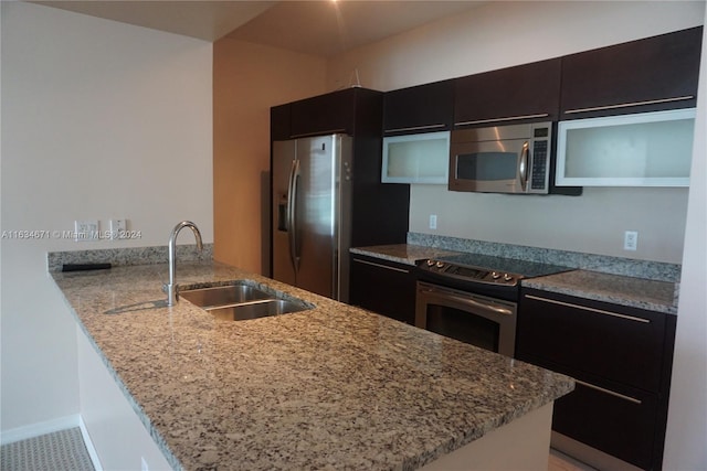 kitchen with stainless steel appliances, sink, kitchen peninsula, and light stone counters