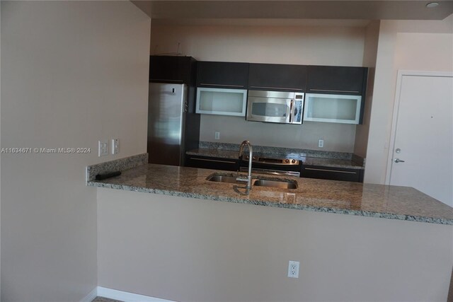 kitchen with kitchen peninsula, dark stone counters, stainless steel appliances, and sink