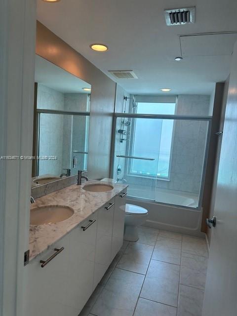 full bathroom featuring combined bath / shower with glass door, toilet, dual bowl vanity, and tile patterned flooring