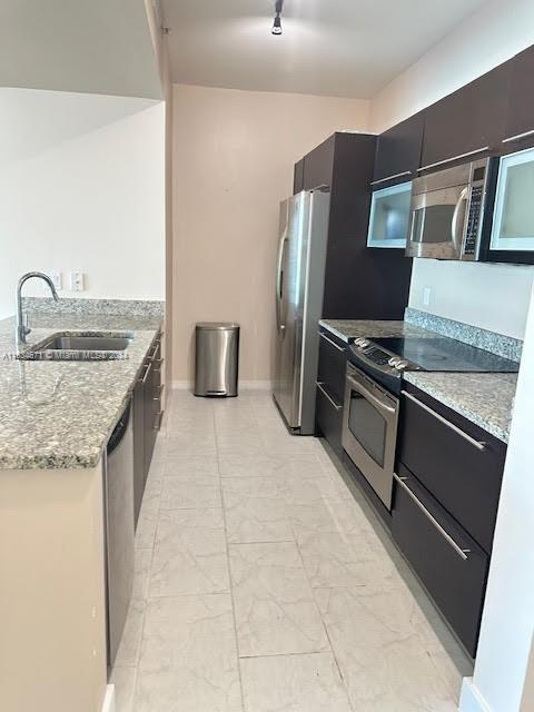 kitchen featuring appliances with stainless steel finishes, light tile patterned floors, sink, and light stone countertops