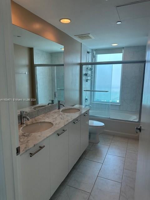 full bathroom with double sink vanity, toilet, bath / shower combo with glass door, and tile patterned floors