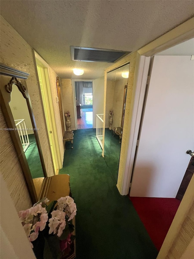 hallway with carpet floors, visible vents, and a textured ceiling