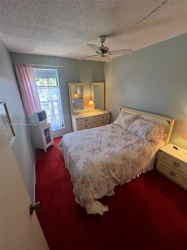 bedroom with ceiling fan, dark carpet, and a textured ceiling