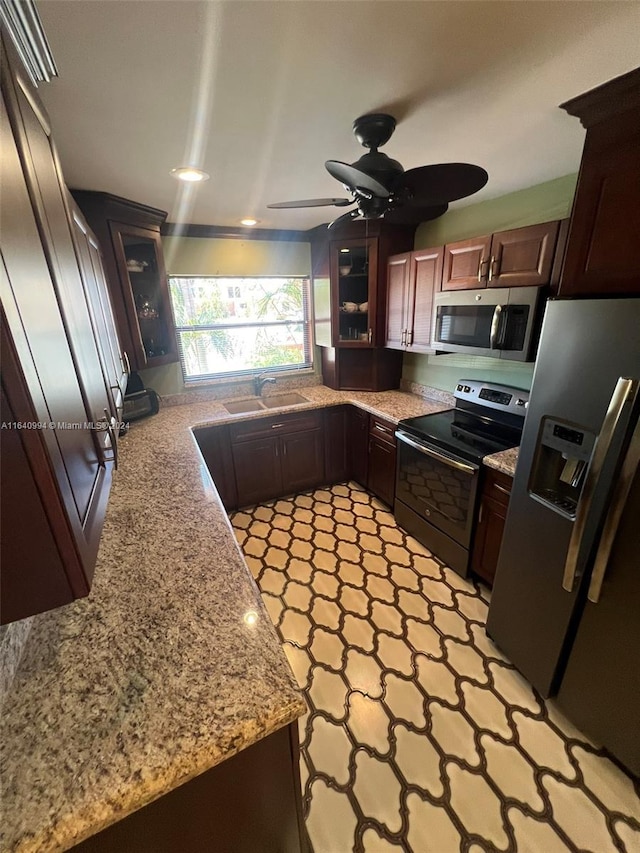 kitchen featuring ceiling fan, light stone counters, stainless steel appliances, a sink, and glass insert cabinets