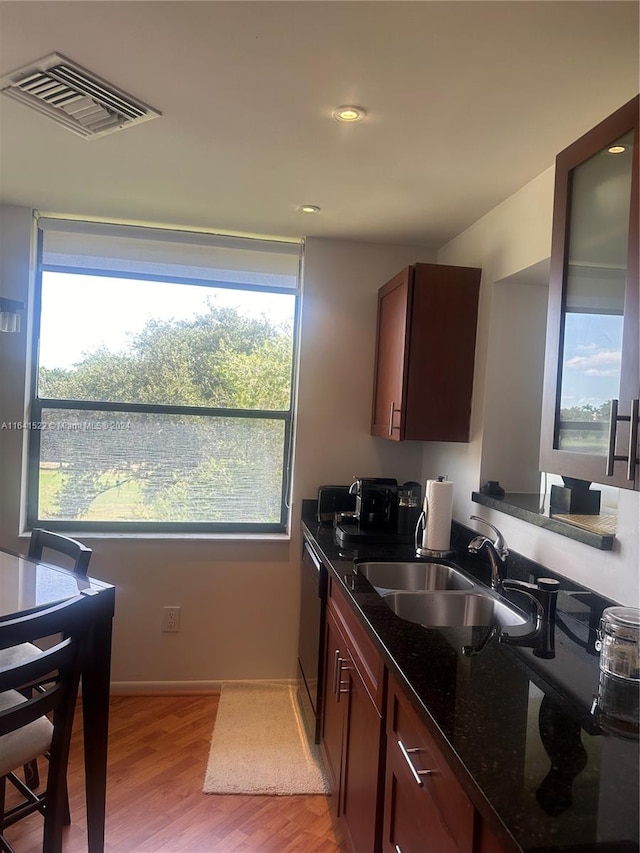 kitchen featuring sink, a healthy amount of sunlight, dark stone countertops, and light hardwood / wood-style floors