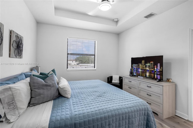 bedroom with ceiling fan, a tray ceiling, and light hardwood / wood-style floors