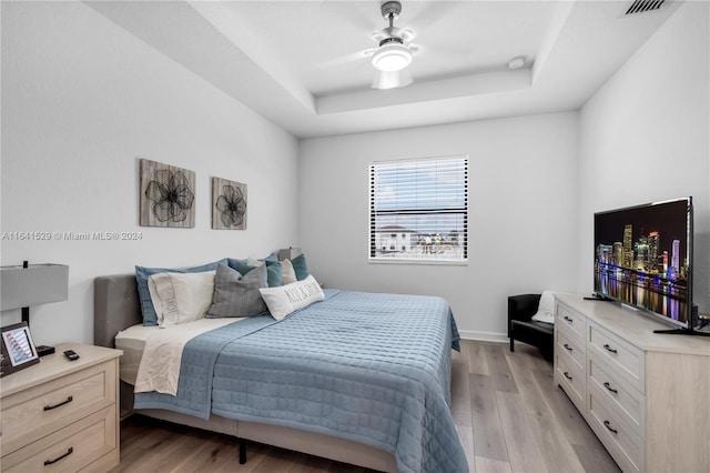 bedroom with a raised ceiling, ceiling fan, and light hardwood / wood-style floors