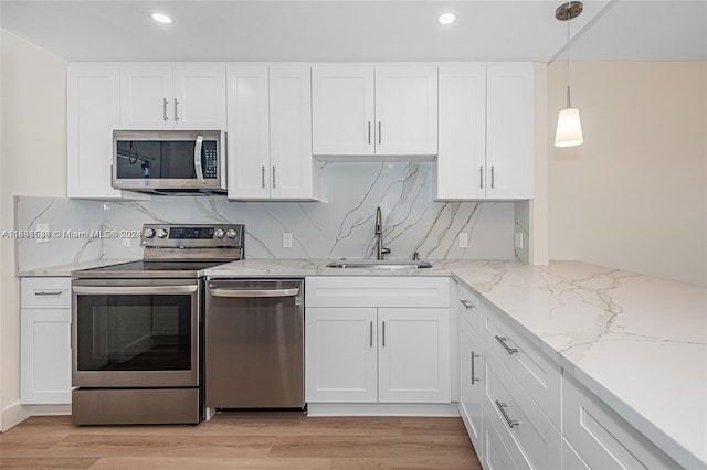 kitchen with pendant lighting, sink, white cabinets, light hardwood / wood-style flooring, and appliances with stainless steel finishes