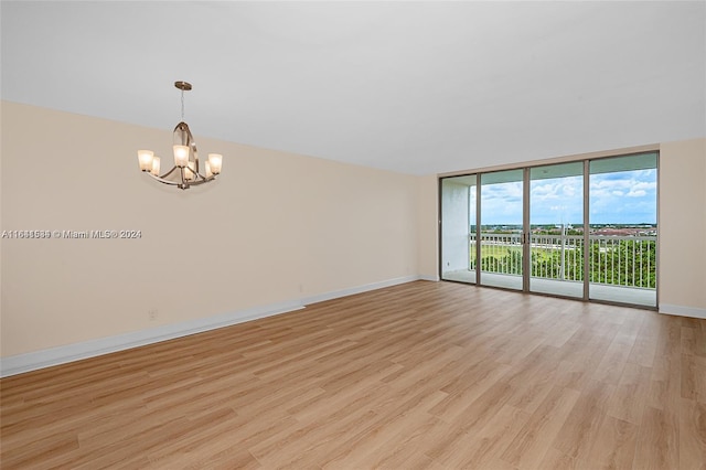 spare room featuring a wall of windows, an inviting chandelier, and light hardwood / wood-style flooring