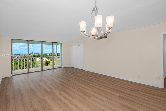 empty room featuring light wood-type flooring, an inviting chandelier, and expansive windows