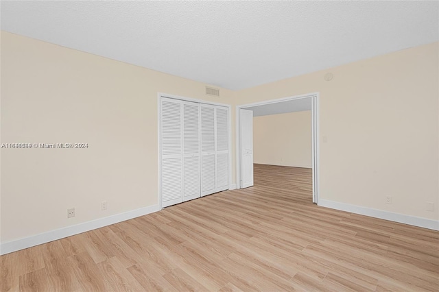 unfurnished bedroom featuring a textured ceiling, light hardwood / wood-style flooring, and a closet