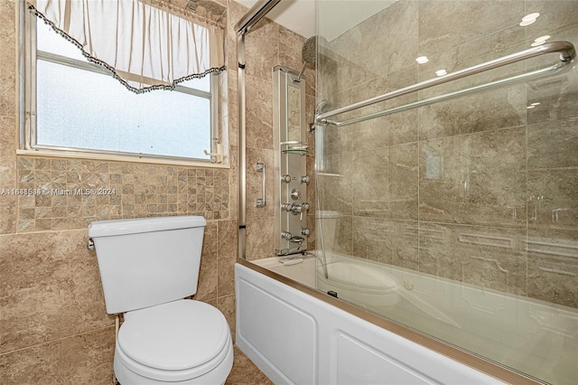 bathroom with tile walls, shower / bath combination with glass door, and toilet