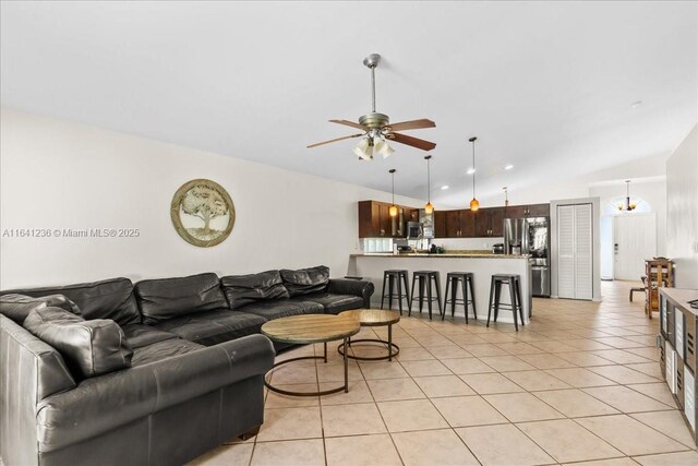 living room featuring ceiling fan with notable chandelier, light tile patterned floors, and lofted ceiling