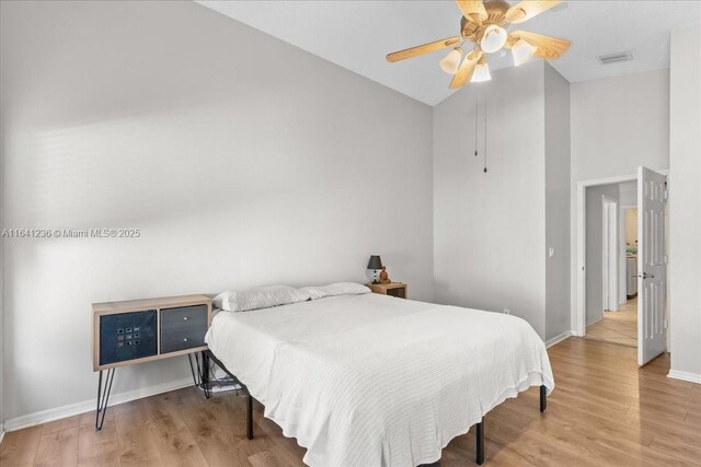 bedroom with hardwood / wood-style floors, ceiling fan, and a high ceiling