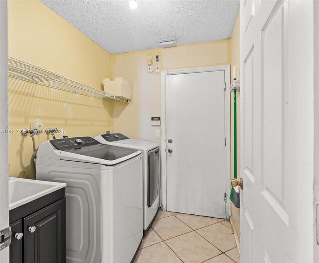 washroom featuring cabinets, washing machine and dryer, a textured ceiling, and light tile patterned flooring