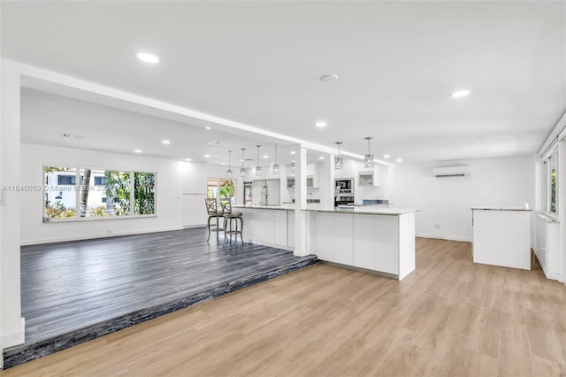 kitchen featuring light wood-type flooring, hanging light fixtures, white cabinets, a kitchen bar, and a wall unit AC