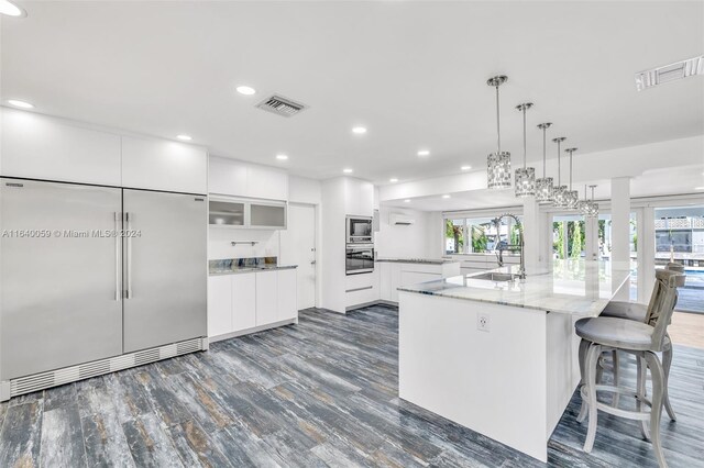 kitchen with built in appliances, white cabinets, dark hardwood / wood-style floors, and a healthy amount of sunlight