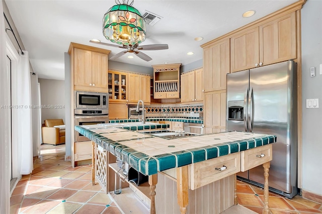 kitchen with a kitchen island with sink, tasteful backsplash, stainless steel appliances, tile countertops, and ceiling fan