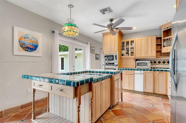 kitchen featuring appliances with stainless steel finishes, decorative backsplash, pendant lighting, ceiling fan, and tile counters