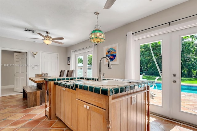 kitchen featuring an island with sink, light brown cabinets, pendant lighting, ceiling fan, and french doors