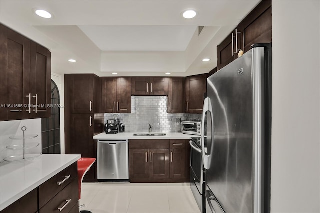 kitchen with light tile patterned flooring, appliances with stainless steel finishes, tasteful backsplash, sink, and a tray ceiling