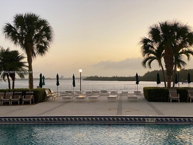 pool at dusk featuring a patio and a water view