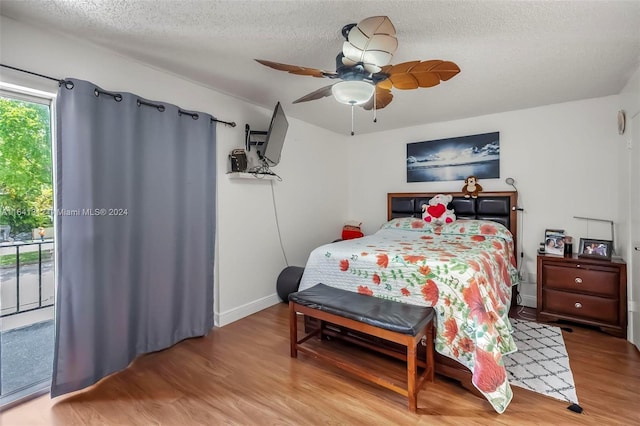 bedroom with access to outside, a textured ceiling, hardwood / wood-style floors, and ceiling fan