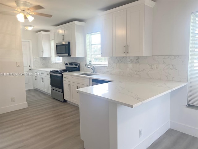 1005 NE 2nd St, Hallandale Beach, FL 33009 - kitchen with a peninsula, a sink, light wood-style floors, white cabinetry, and appliances with stainless steel finishes