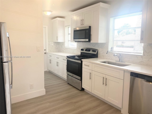 kitchen with white cabinets, sink, tasteful backsplash, light hardwood / wood-style floors, and stainless steel appliances