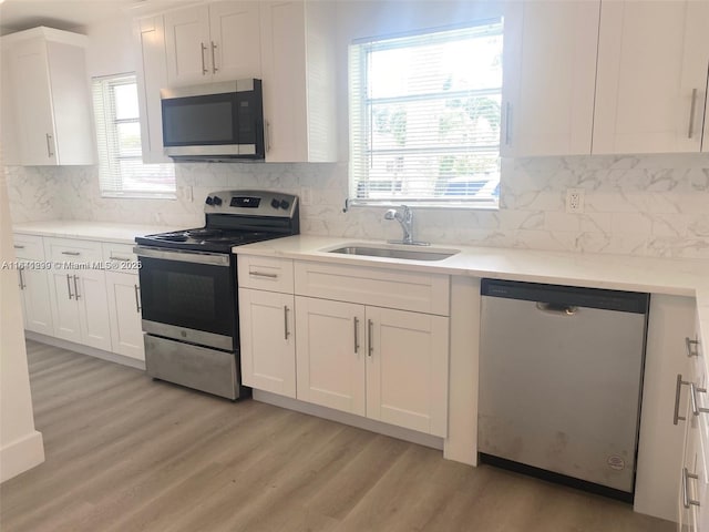 kitchen with backsplash, light wood-type flooring, stainless steel appliances, sink, and white cabinetry