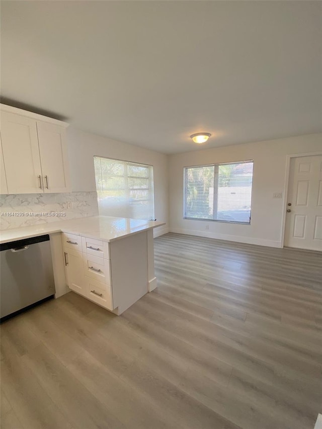 kitchen with tasteful backsplash, white cabinets, stainless steel dishwasher, and light hardwood / wood-style floors