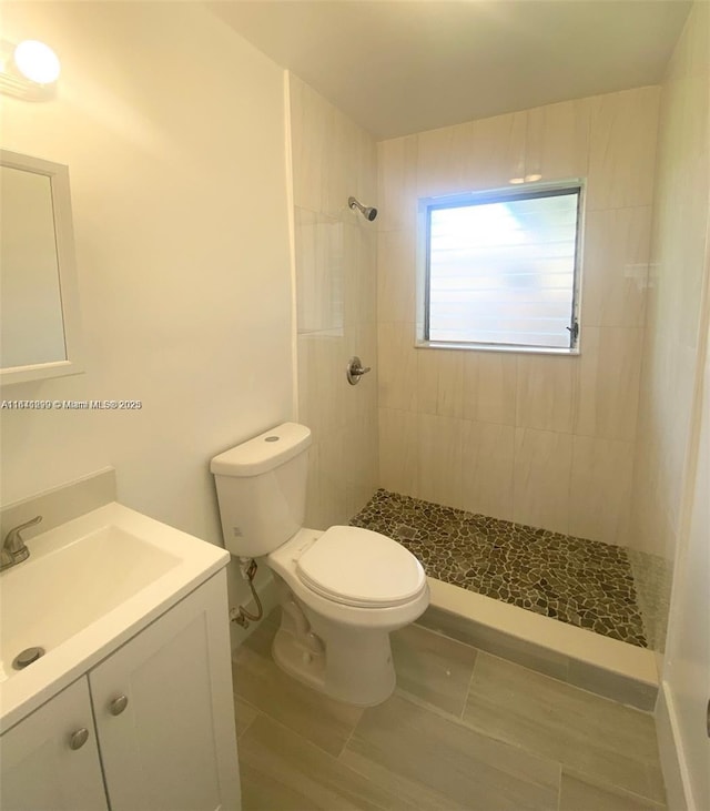 bathroom featuring tiled shower, tile patterned floors, vanity, and toilet