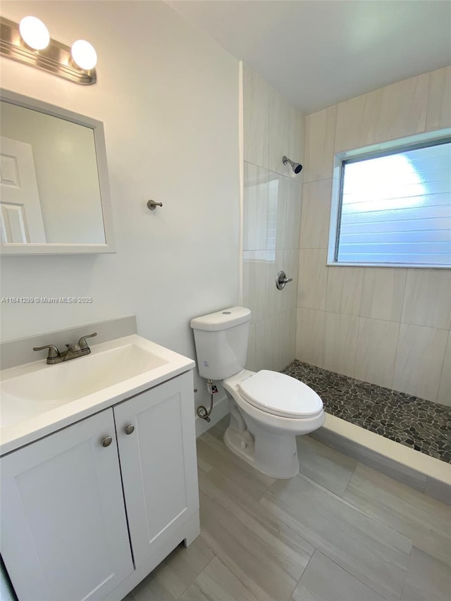 bathroom with tiled shower, vanity, and toilet