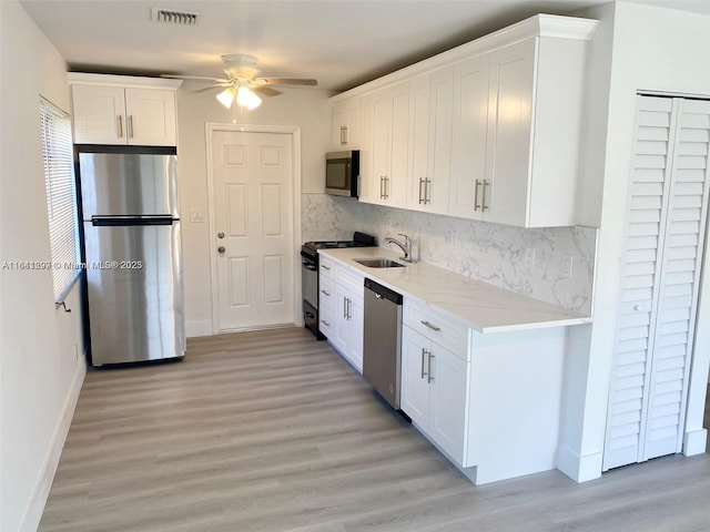 kitchen with white cabinetry, sink, tasteful backsplash, light hardwood / wood-style floors, and appliances with stainless steel finishes