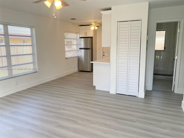 kitchen featuring stainless steel refrigerator, white cabinetry, ceiling fan, and light wood-type flooring