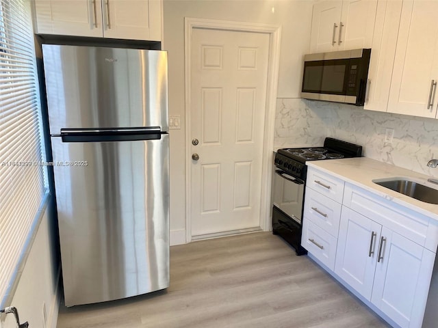 kitchen featuring sink, tasteful backsplash, appliances with stainless steel finishes, white cabinets, and light wood-type flooring