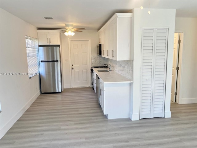 kitchen featuring white cabinets, stainless steel appliances, light hardwood / wood-style flooring, and tasteful backsplash