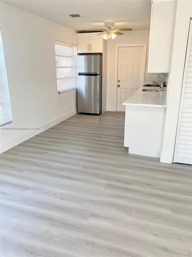 kitchen with white cabinets, sink, ceiling fan, stainless steel fridge, and decorative backsplash