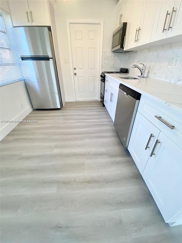 kitchen with white cabinetry, sink, light stone counters, decorative backsplash, and appliances with stainless steel finishes