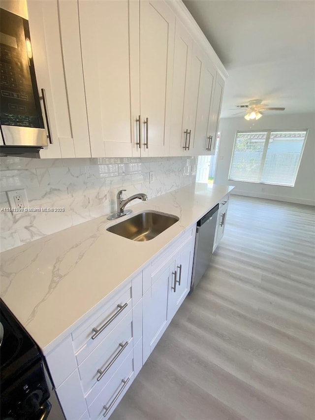 kitchen featuring light stone countertops, light wood-type flooring, stainless steel dishwasher, sink, and white cabinets