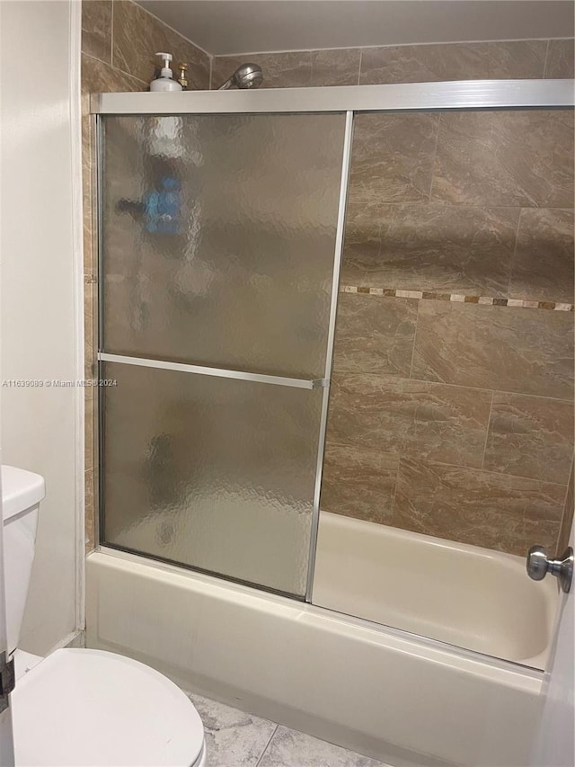 bathroom with bath / shower combo with glass door, tile patterned flooring, and toilet