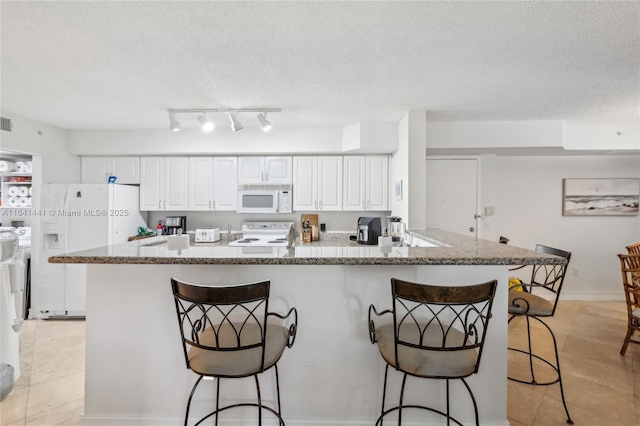 kitchen with a textured ceiling, white appliances, a breakfast bar, white cabinetry, and light stone countertops